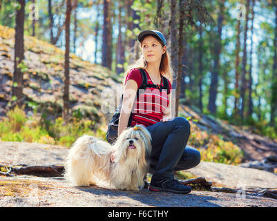 Jeune touriste assis sur la pierre avec chien dans la forêt d'été. Banque D'Images