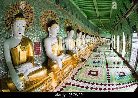 SAGAING, Myanmar — debout sur une colline à Sagaing, la pagode OoHminThoneSel présente une longue alcôve incurvée bordée de dizaines de statues du Bouddha. Après de récentes rénovations et améliorations en cours rendues possibles par des donateurs, la pagode est richement décorée avec des mosaïques de carreaux colorés et de la peinture fraîche et brillante. Banque D'Images