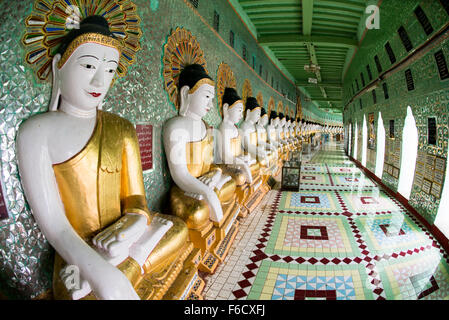 SAGAING, Myanmar — debout sur une colline à Sagaing, la pagode OoHminThoneSel présente une longue alcôve incurvée bordée de dizaines de statues du Bouddha. Après de récentes rénovations et améliorations en cours rendues possibles par des donateurs, la pagode est richement décorée avec des mosaïques de carreaux colorés et de la peinture fraîche et brillante. Banque D'Images