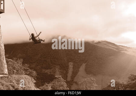 Silhouette d'une jeune femme heureuse sur une balançoire, se balançant au dessus de la chaîne montagneuse des Andes, Casa del Arbol, Equateur, Style noir et blanc Banque D'Images