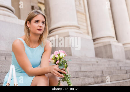 Sad girl sitting on steps tenant un bouquet de fleurs Banque D'Images