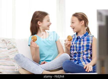 Happy girls watching TV and eating cookies à la maison Banque D'Images