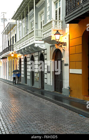 Deux hommes avec parapluie marcher par façades coloniales espagnoles et pavés, Old San Juan, Puerto Banque D'Images