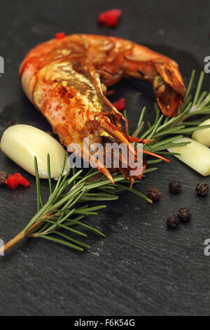 Crevettes géantes grillées ensemble avec le romarin, l'ail et le piment rouge sur un fond en ardoise noire. Banque D'Images