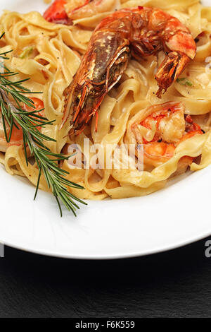 Un plat de pâtes aux crevettes frits sur une plaque blanche, garni de romarin. Banque D'Images