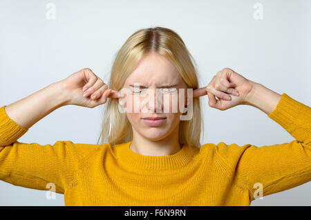 Close up dégoûté Jeune femme couvrant ses oreilles avec les doigts, avec les yeux fermés, contre un arrière-plan gris. Banque D'Images