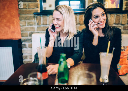 Deux belles femmes parlant au téléphone dans le café tout en étant heureux Banque D'Images