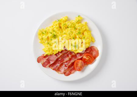 Assiette d'œufs brouillés et de tranches de lard grillé sur fond blanc Banque D'Images