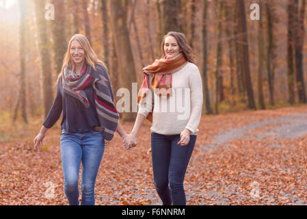 Deux femmes joyeux en marche main dans la main à travers un parc boisé de l'automne avec les feuilles colorées sur le sol dans une saine lifesty Banque D'Images