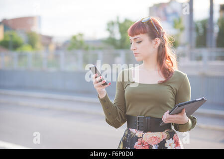 Demi-longueur de jeunes beau portrait femme rousse à l'aide d'un smartphone, à la recherche et à la baisse sur l'écran en maintenant Banque D'Images