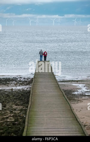 Une femme et un homme âgés se tiennent sur une jetée de Llandudno, au Pays de Galles, en face de Gwynt y Mor parc éolien offshore en mer d'Irlande. Banque D'Images