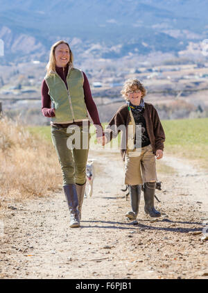 Belle Mère, jeune fils et des chiens de marcher le long chemin de terre sur ranch Banque D'Images