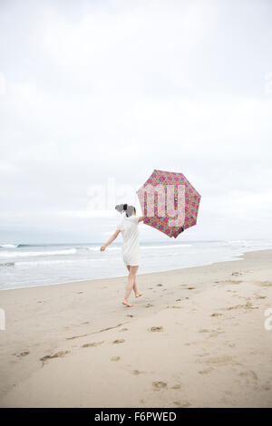Femme marche dans le vent avec umbrella on beach Banque D'Images