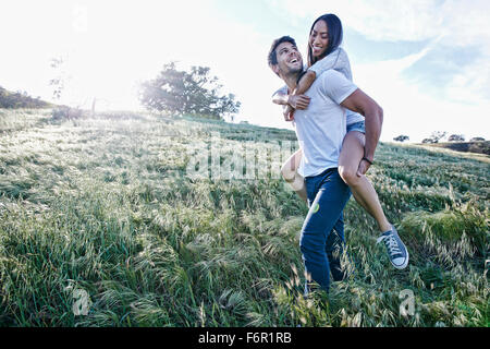 Man carrying girlfriend piggyback in field Banque D'Images