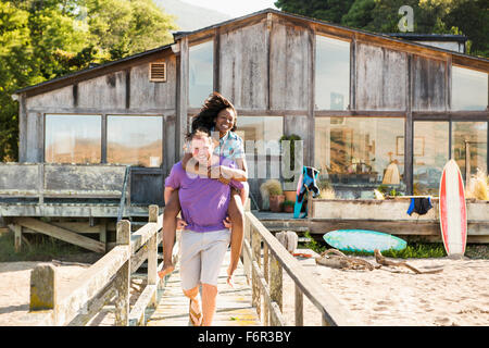 Man carrying girlfriend piggyback sur terrasse en bois Banque D'Images