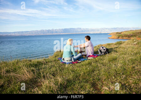 Jeune couple ayant un pique-nique sur le bord de l'eau Banque D'Images