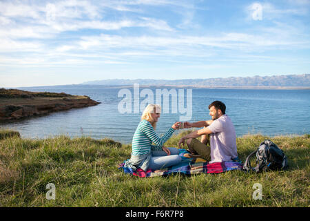 Jeune couple ayant un pique-nique sur le bord de l'eau Banque D'Images