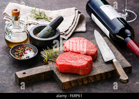 Frais crus de viande marbrée Steaks avec les assaisonnements et bouteille de vin rouge sur fond sombre Banque D'Images