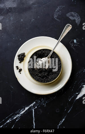 Caviar noir d'esturgeon dans pouvez et cuillère sur fond de marbre noir Banque D'Images