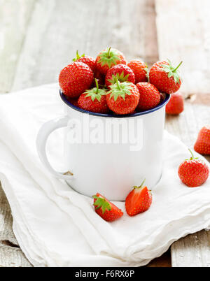 Un mug blanc rempli de succulentes fraises rouge frais mûrs juteux sur une vieille table en bois haut texturé Banque D'Images