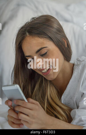 Caucasian woman using cell phone in bed Banque D'Images