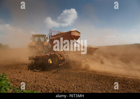 La poussière qu'il crée du tracteur remorque une grand semoir derrière elle tandis que les semis de graines. Banque D'Images