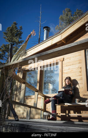 Caucasian woman reading book on cabin porch Banque D'Images