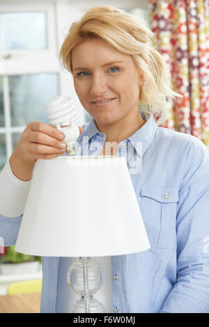 Woman Putting Low Energy Lightbulb en voyant à l'accueil Banque D'Images