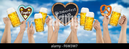 Beaucoup de mains tenant l'allemand de la bière (Oktoberfest) et d'épices en forme de coeur tableau noir sur bleu ciel nuageux Banque D'Images