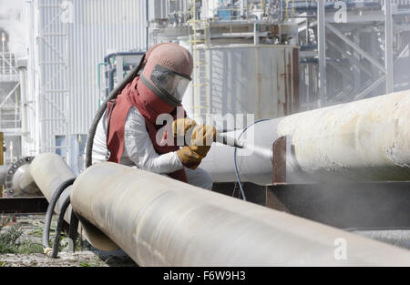 Un travailleur utilise un jet haute pression pour nettoyer les tuyaux de la pétrochimie Banque D'Images