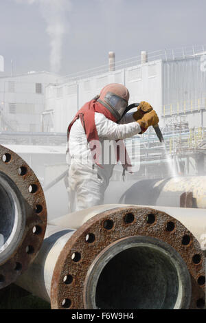 Un travailleur utilise un jet haute pression pour nettoyer les tuyaux de la pétrochimie Banque D'Images