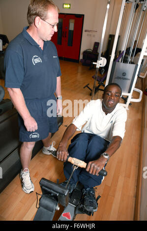 L'accès aux services, instructeur de conditionnement physique et l'homme handicapé dans la salle de sport ; à l'aide d'une machine à ramer, Banque D'Images