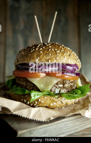 Gourmet burger au fromage fondu, la tomate et l'oignon le remplissage en haut d'une planche à découper en bois Banque D'Images