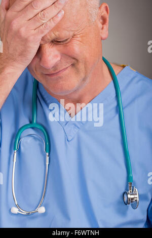 Médecin affolé wearing blue scrubs, avec sa main sur sa tête et le visage. Banque D'Images