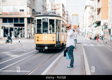 Beau jeune homme d'affaires à tête de race blanche debout sur un arrêt de bus, à sa montre-bracelet - retard, d'attente, travail concept Banque D'Images