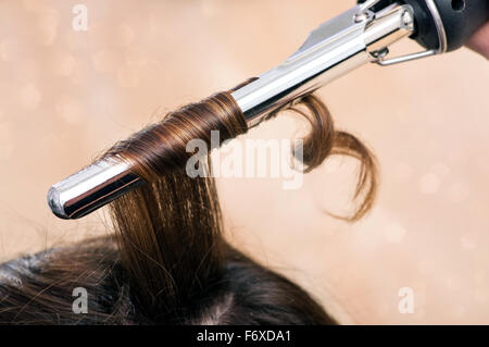 Hairstylist à l'aide d'un fer à friser à ferme anglaises dans les longs cheveux bruns d'une cliente Banque D'Images
