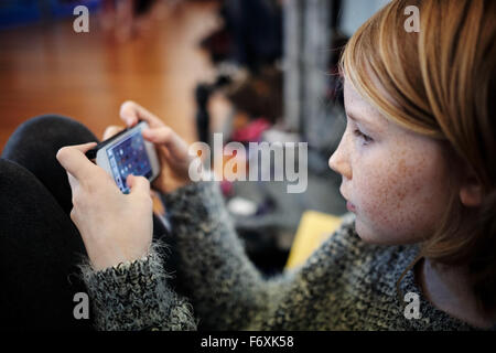 Jeune fille blonde jouant sur téléphone mobile device Banque D'Images