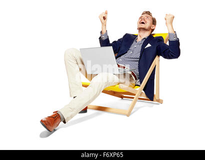 Portrait de jeune homme satisfait assis sur des transats. Il lève les bras en signe de victoire. Banque D'Images
