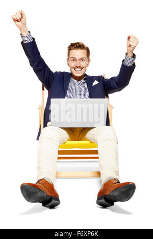 Portrait de jeune homme satisfait assis sur des transats. Il lève les bras en signe de victoire. Banque D'Images