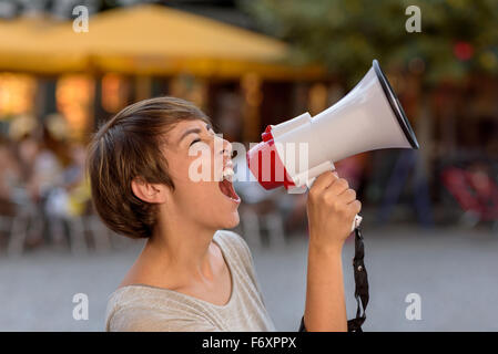 Jeune femme en colère crier dans un mégaphone comme elle se tient sur une rue urbaine ses frustrations d'évacuation lors d'un rassemblement en plein air Banque D'Images
