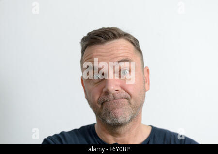 Sans voix middle-aged man looking at camera non rasé avec des yeux bleus et l'expression du visage perplexe, portrait avec copie espace o Banque D'Images