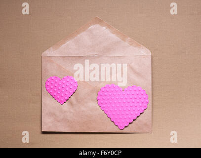 Deux coeurs roses sur du papier craft envelopper sur fond brun. Banque D'Images