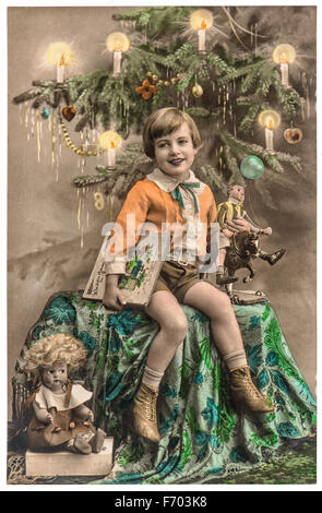 Happy boy avec arbre de Noël, cadeaux et jouets vintage. Photo ancienne originale avec du grain de film et des rayures Banque D'Images