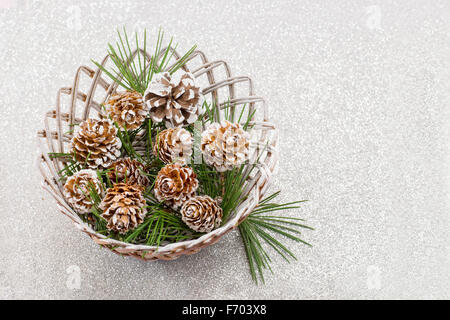 La neige a couvert des pommes de pin dans un bol en osier en bois sur fond brillant Banque D'Images