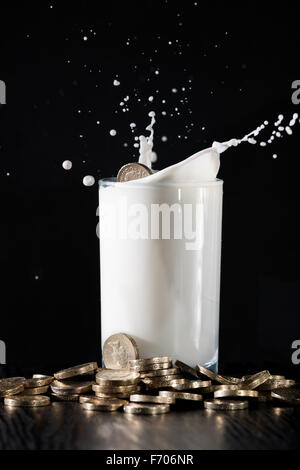 Pièce d'une livre tombé dans un verre de lait sur une table empilé avec de l'argent. Banque D'Images