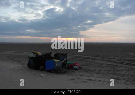 Débris marins en plastique, y compris wheelie-poubelles, entassés sur la plage de sable vers les nuages gris de soleil rouge, St Annes, Fylde Coast, UK Banque D'Images