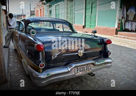 S'appuyant sur conducteur garé vintage car ayant une pause cigarette à l'ombre sur une rue pavée ensoleillée dans le sud-ouest de Cuba Trinidad Banque D'Images