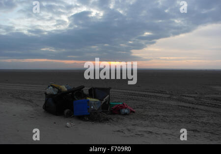 Des tas de débris en plastique, y compris wheelie-poubelles, sur la plage de sable vers les nuages gris de soleil rouge, St Annes, Fylde Coast, UK Banque D'Images