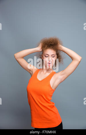 Amusant drôle certain jeune femme frisée émotionnelle en orange top pose, jouant avec les cheveux et faire une grimace Banque D'Images