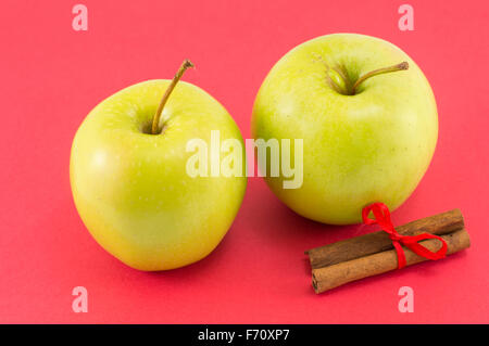 Des pommes fraîches et des bâtons de cannelle avec un ruban sur fond rouge Banque D'Images